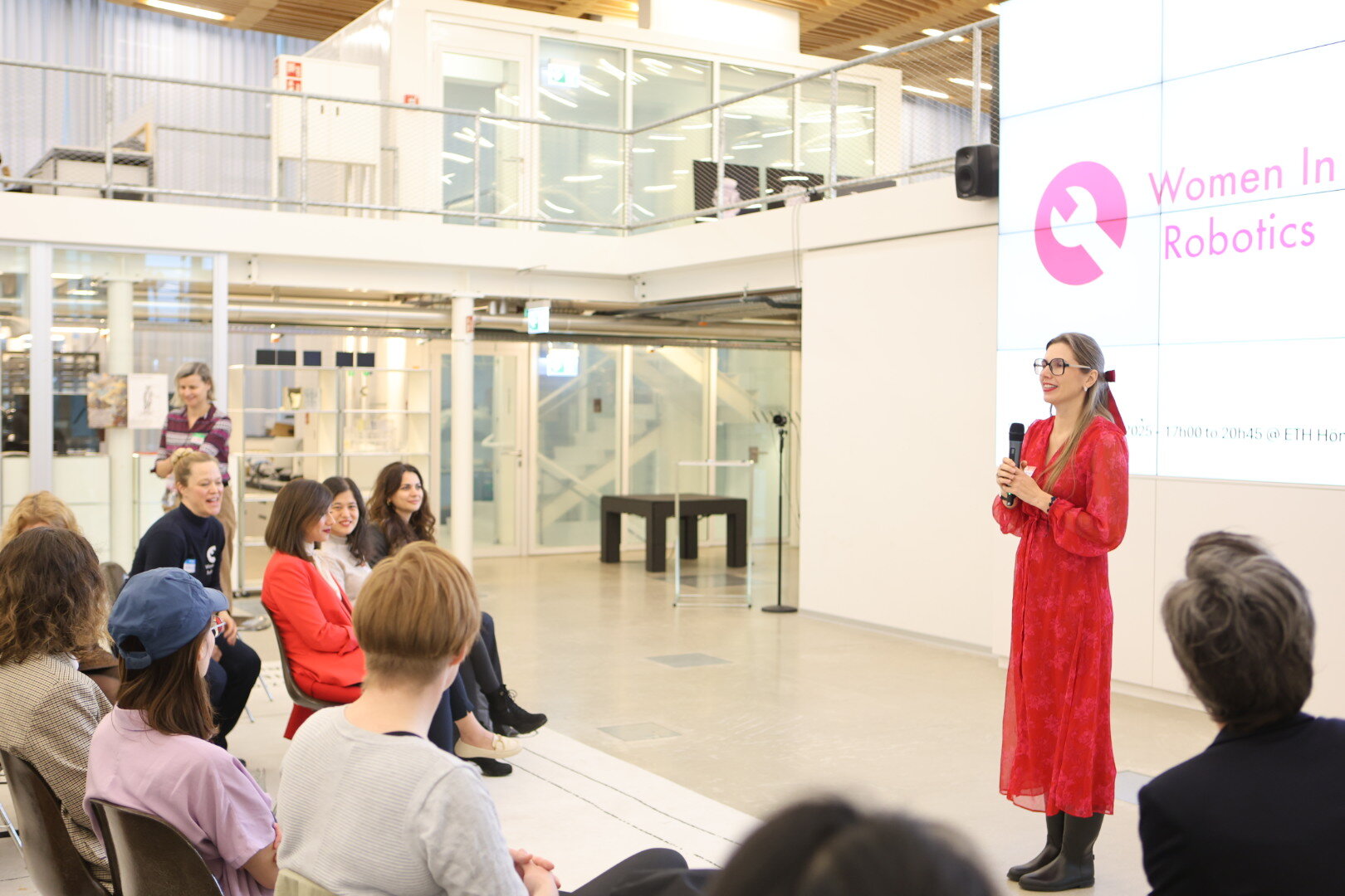 Kateryna Portmann speaking to the Women in Robotics community in a red dress, presenting in front of a screen